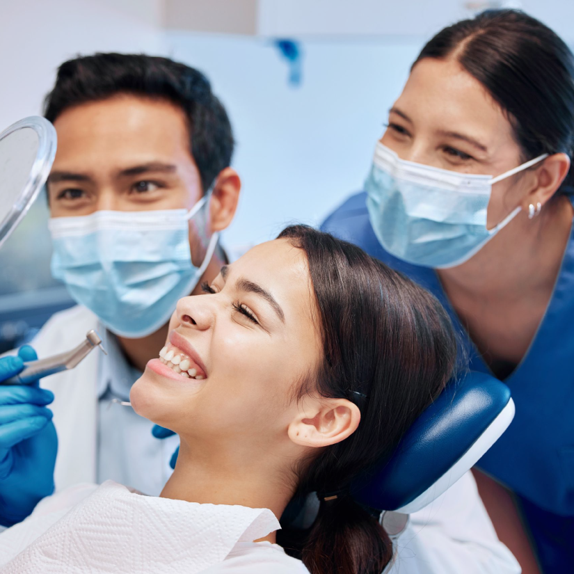 Patiente qui admire son sourire dans un miroir avec le dentiste et l'assistante