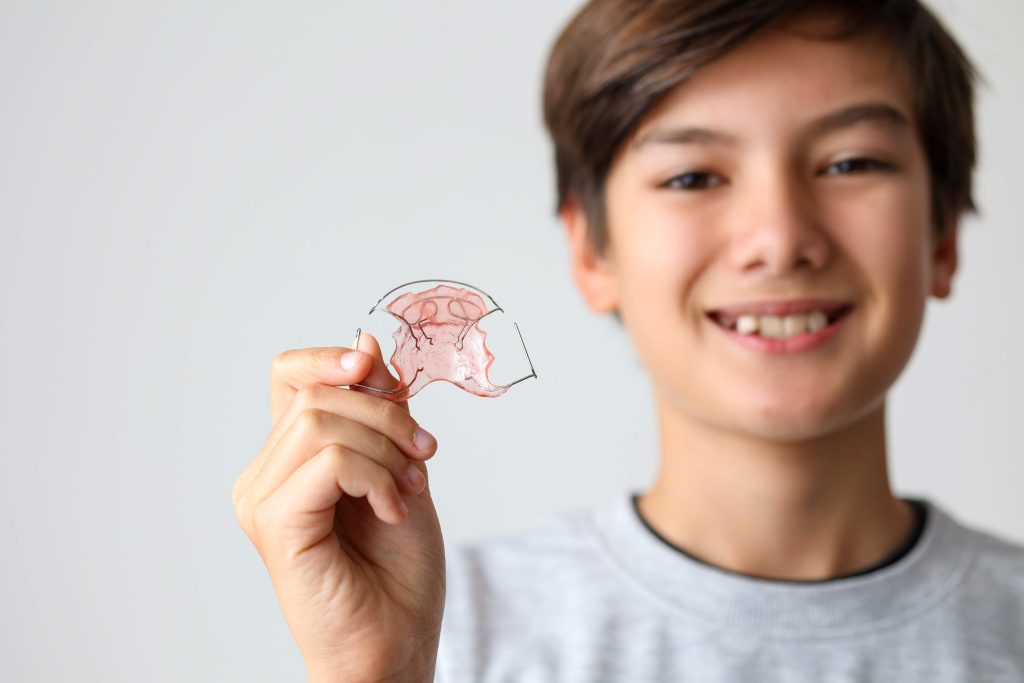 Garçon souriant tenant un appareil dentaire - Orthodontie pour enfants à Lancy (Genève)