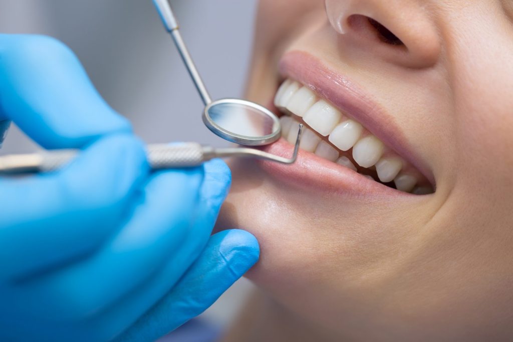 Gros plan d’un détartrage dentaire réalisé par un professionnel avec des instruments de soins bucco-dentaires.